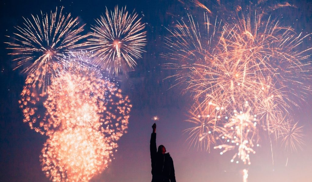 Fireworks behind a kid holding a sparkler